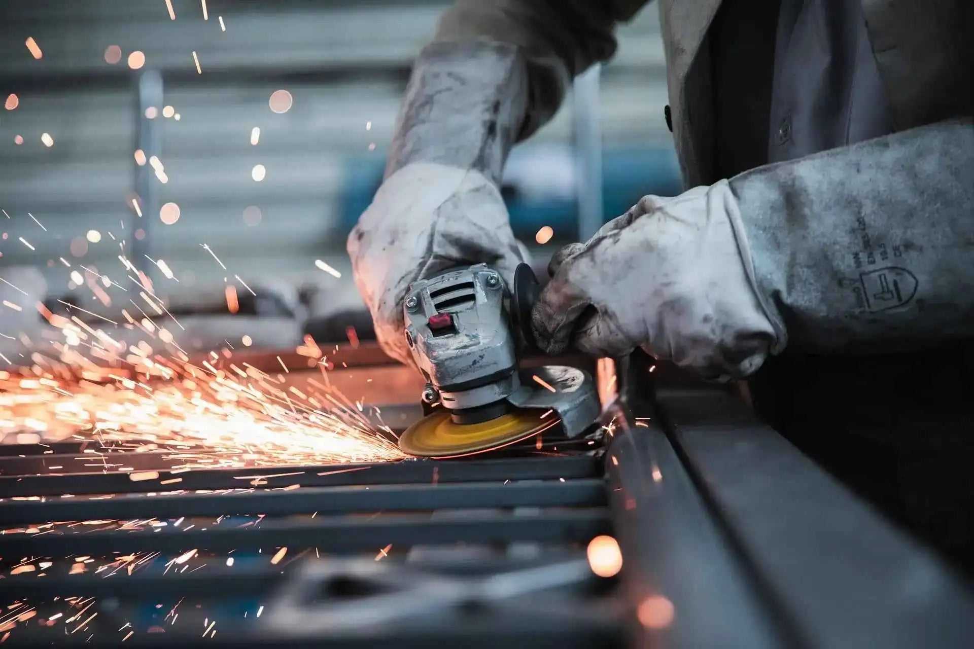 Worker using angle grinder on metal with sparks, wearing protective gloves in industrial setting