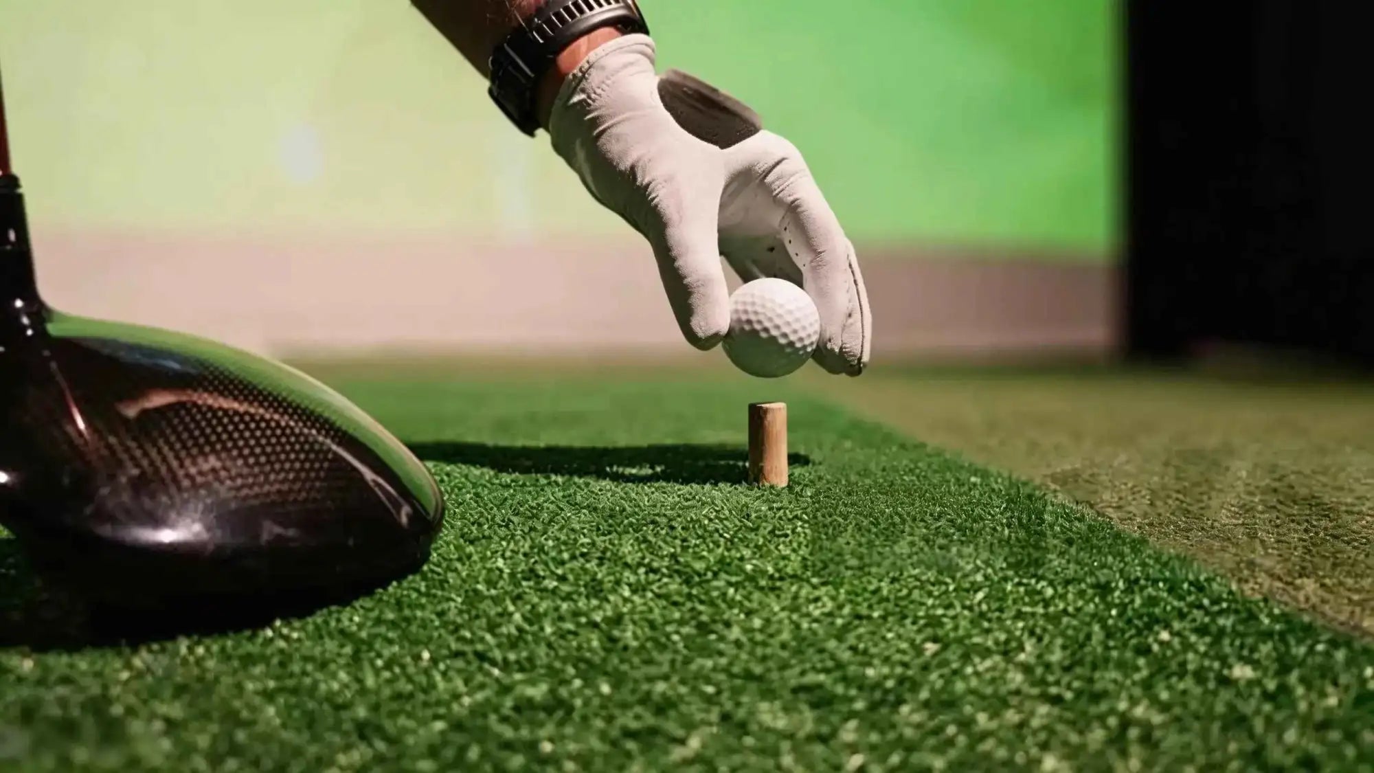 Golfer wearing glove placing golf ball on tee with driver on green turf