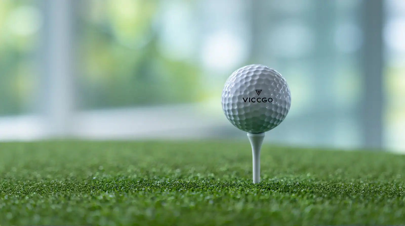 A white vicc go golf ball with a dimpled texture and black branding sits balanced on a tee atop artificial green turf.